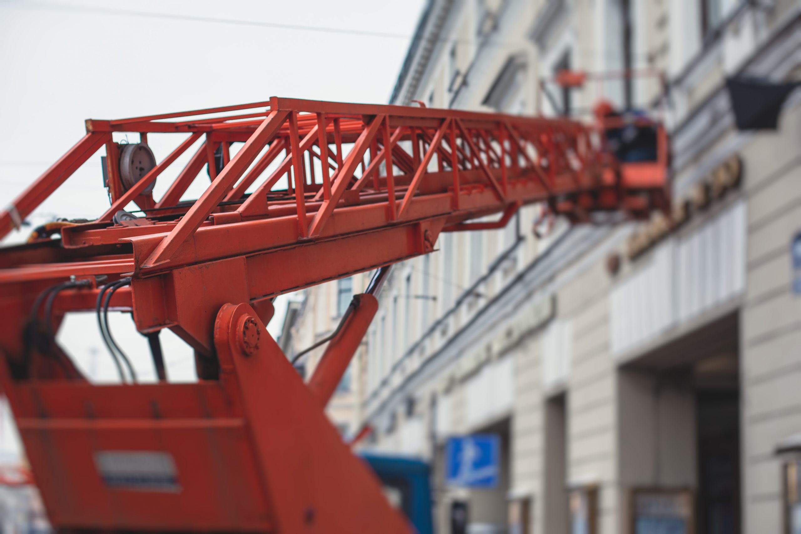 Aerial work platform vehicle during facade decoration, orange telescopic elevator on construction site, rental AWP working in the city streets, engineer working on heights